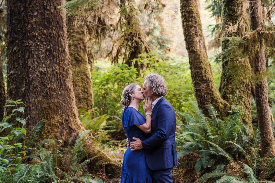 A bride and groom kiss while standing on a trail in a rainforest along the Washington coast