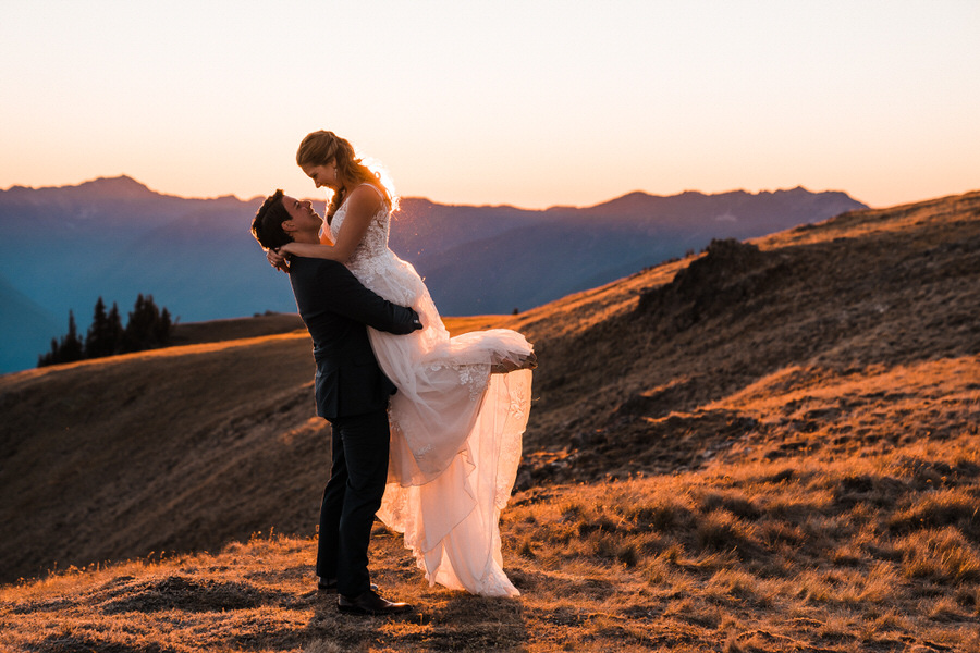 A groom lifts up his bride at sunset with the Olympic Mountains in the background