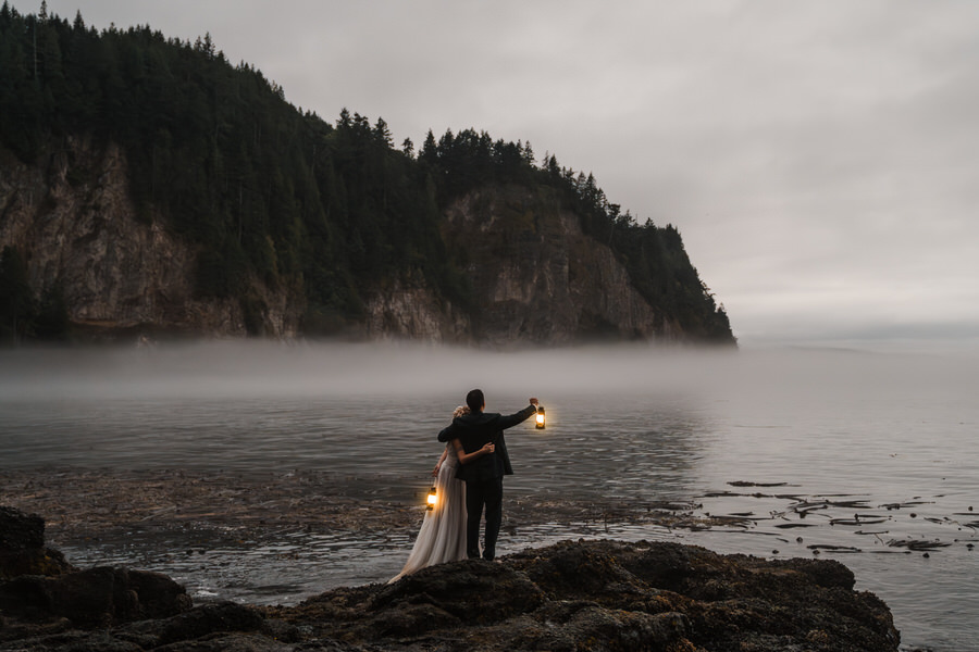 a couple holds lanterns on a foggy coast after their agate beach micro wedding